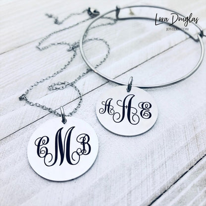 A silver monogram necklace with an engraved initial pendant laid out on a marble surface.
