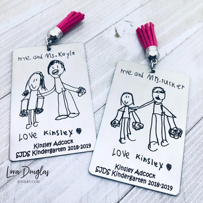 A custom stainless steel bookmark with a laser engraved child's drawing, presented next to its navy blue velvet drawstring pouch.