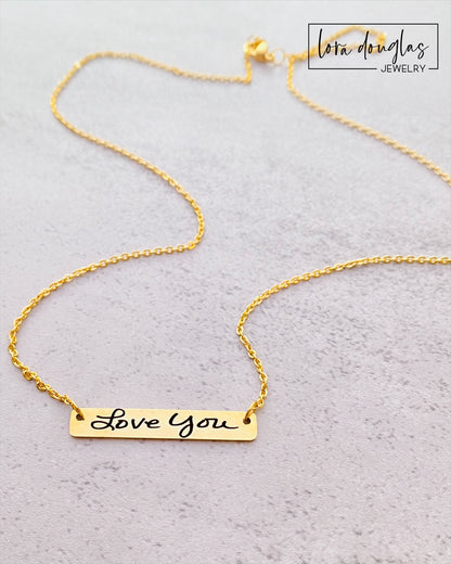 A gold bar necklace with engraved handwriting on it
minimalist engraved handwriting jewelry gift for women