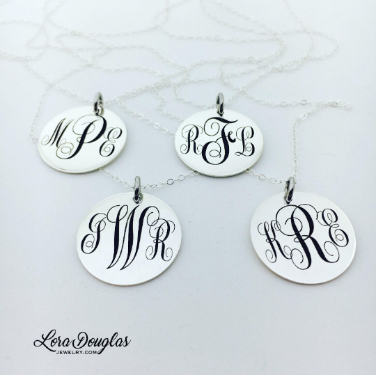 A silver monogram necklace with an engraved initial pendant laid out on a marble surface.