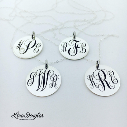 A silver monogram necklace with an engraved initial pendant laid out on a marble surface.