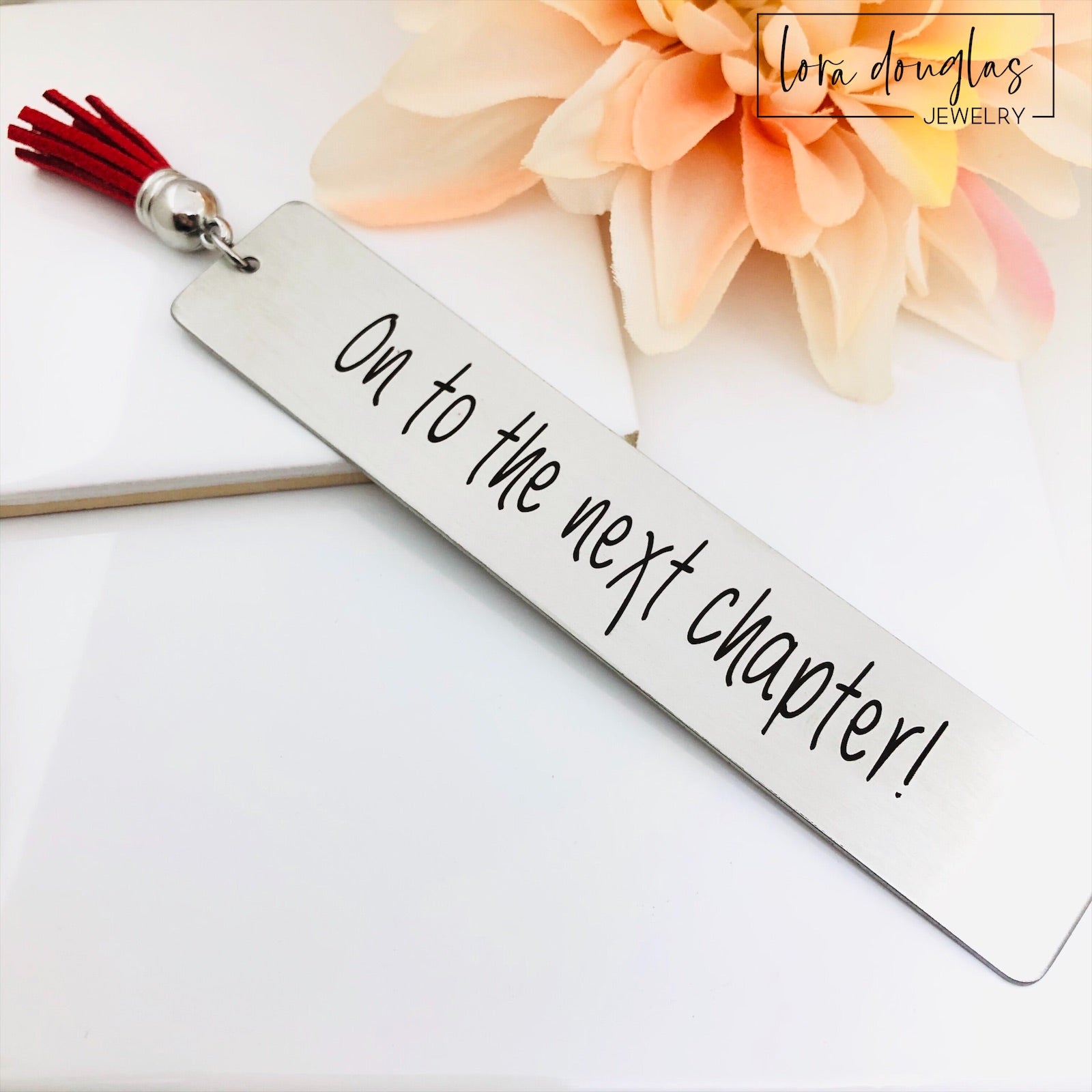 on to the next chapter bookmark engraved on stainless steel metal bookmark with leather tassel, inspirational graduation gift displayed inside open book with permanent laser engraving and brushed silver finish