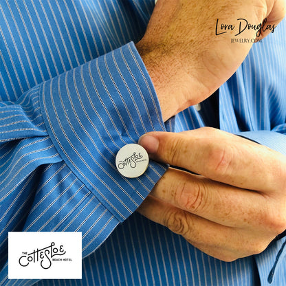 A close-up of a man's sleeve with a striped blue and white shirt, featuring an engraved cufflink with a logo