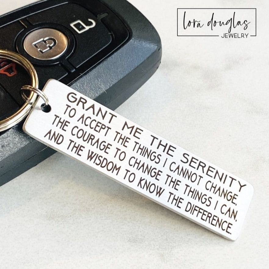 Stainless steel engraved Serenity Prayer keychain attached to car keys, featuring permanent laser engraving on a slim rectangular plaque measuring 2 inches long. Durable tarnish resistant metal keychain includes standard key ring and optional two sided personalization, making a meaningful recovery gift, encouragement keepsake, or inspirational driver accessory.